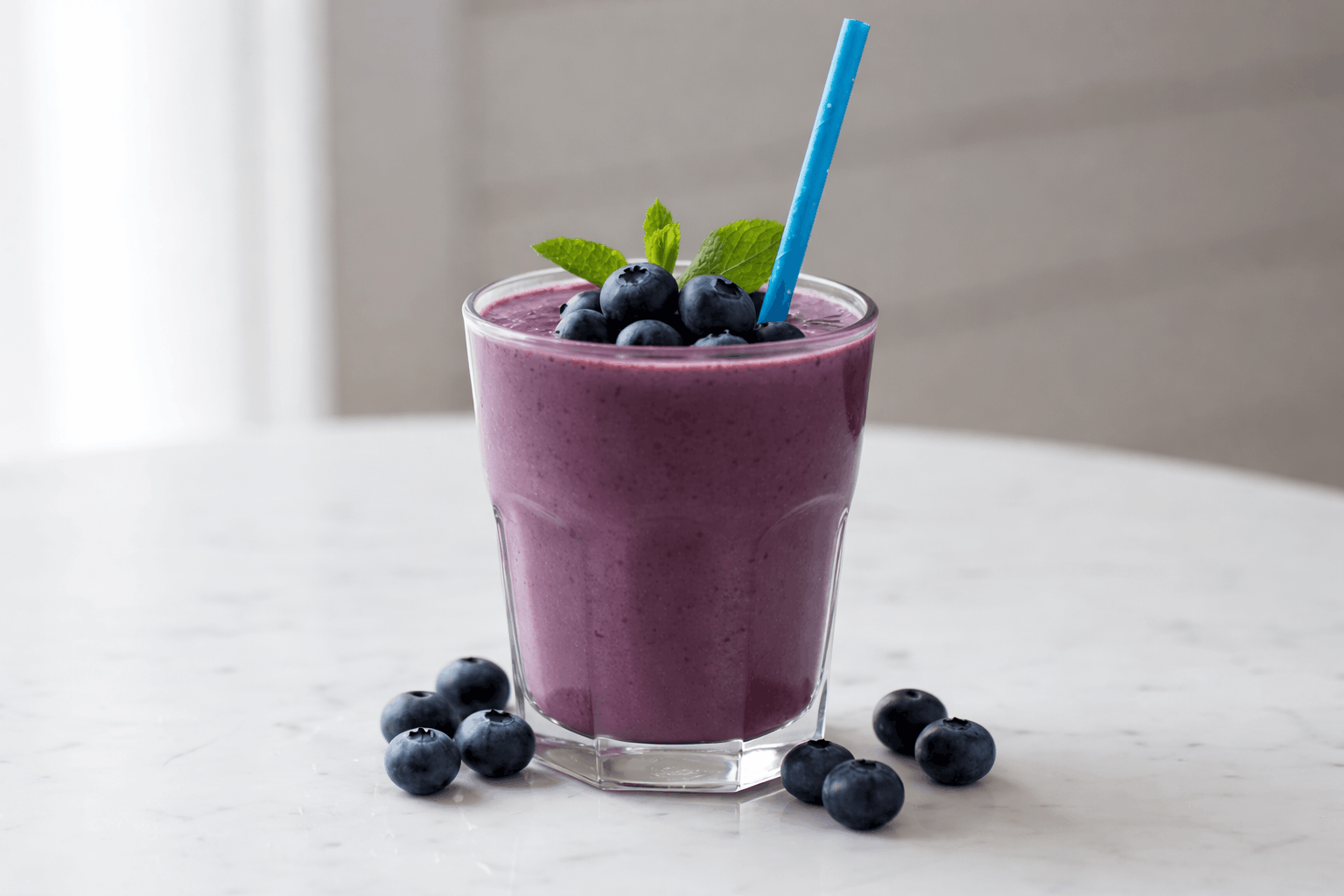 Blaubeer-Protein-Smoothie mit Wildheidelbeeren in einem Glas auf hellem Tisch, dekoriert mit frischen Blaubeeren und Minze.